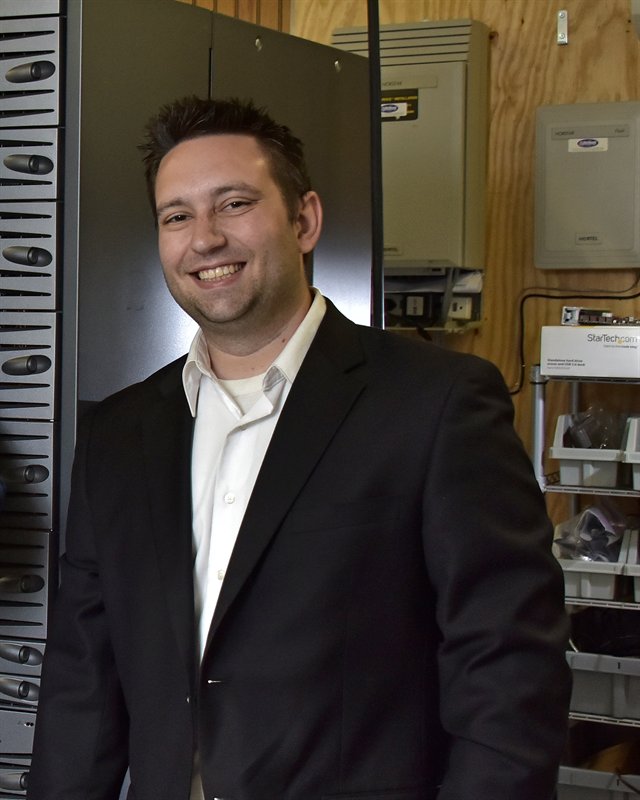 Christopher Powers, founder of Powers Computing, standing beside a server rack.